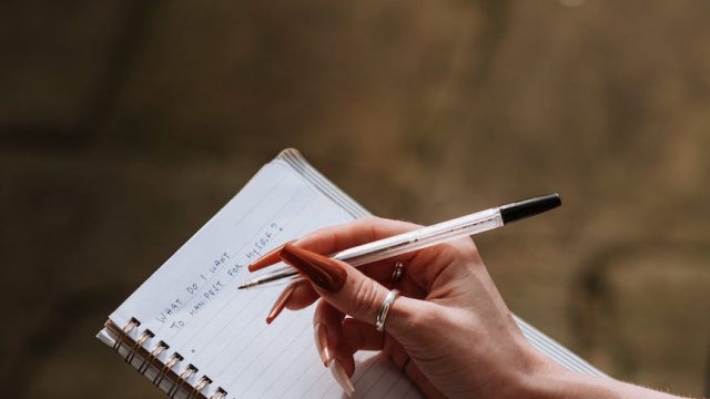 woman with long manicure taking notes in copybook